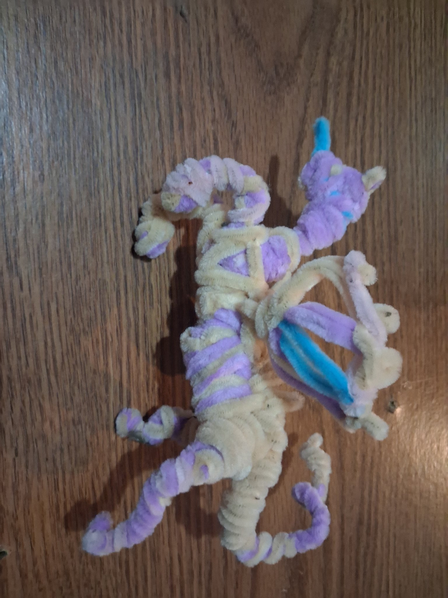 Handmade purple, cream and blue pipe-cleaner unicorn on a wooden surface