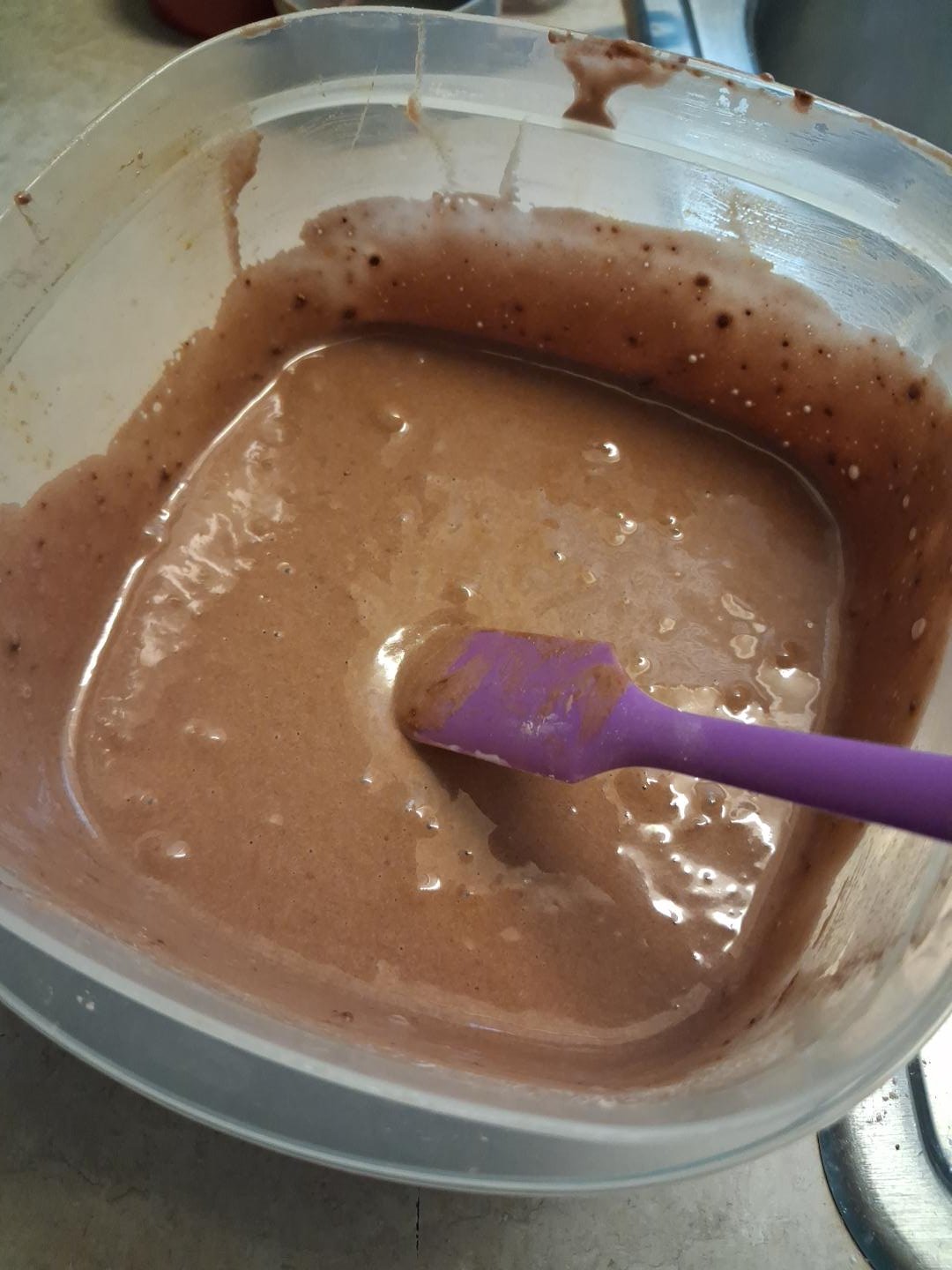 Chocolate batter in a mixing container with a purple spatula