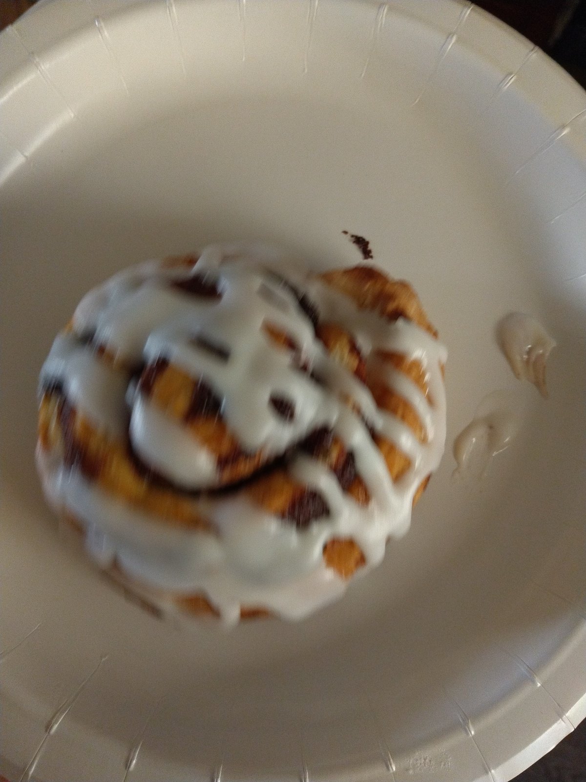 Iced cinnamon roll on a white plate
