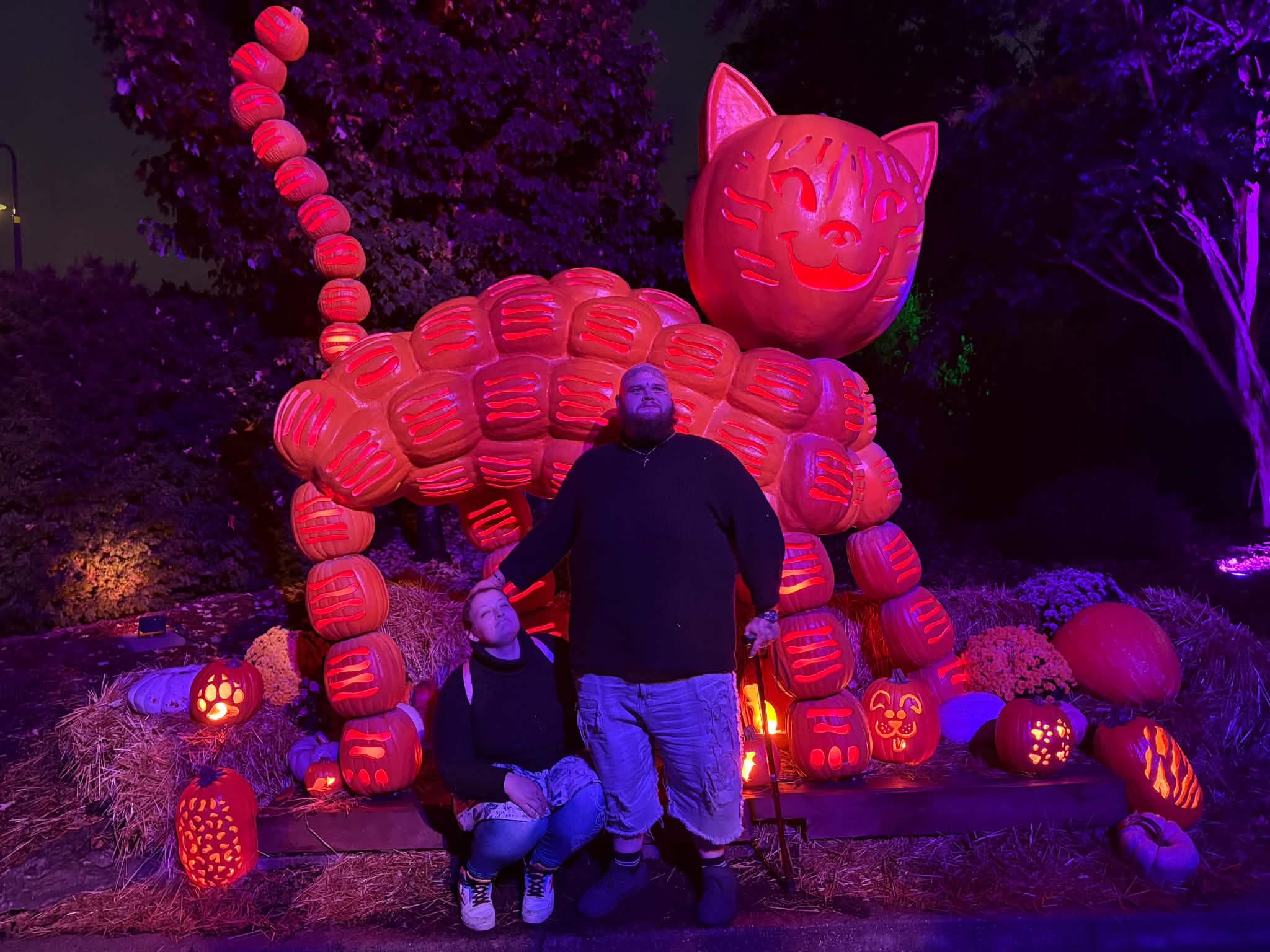 Two people posing with the giant glowing pumpkin cat