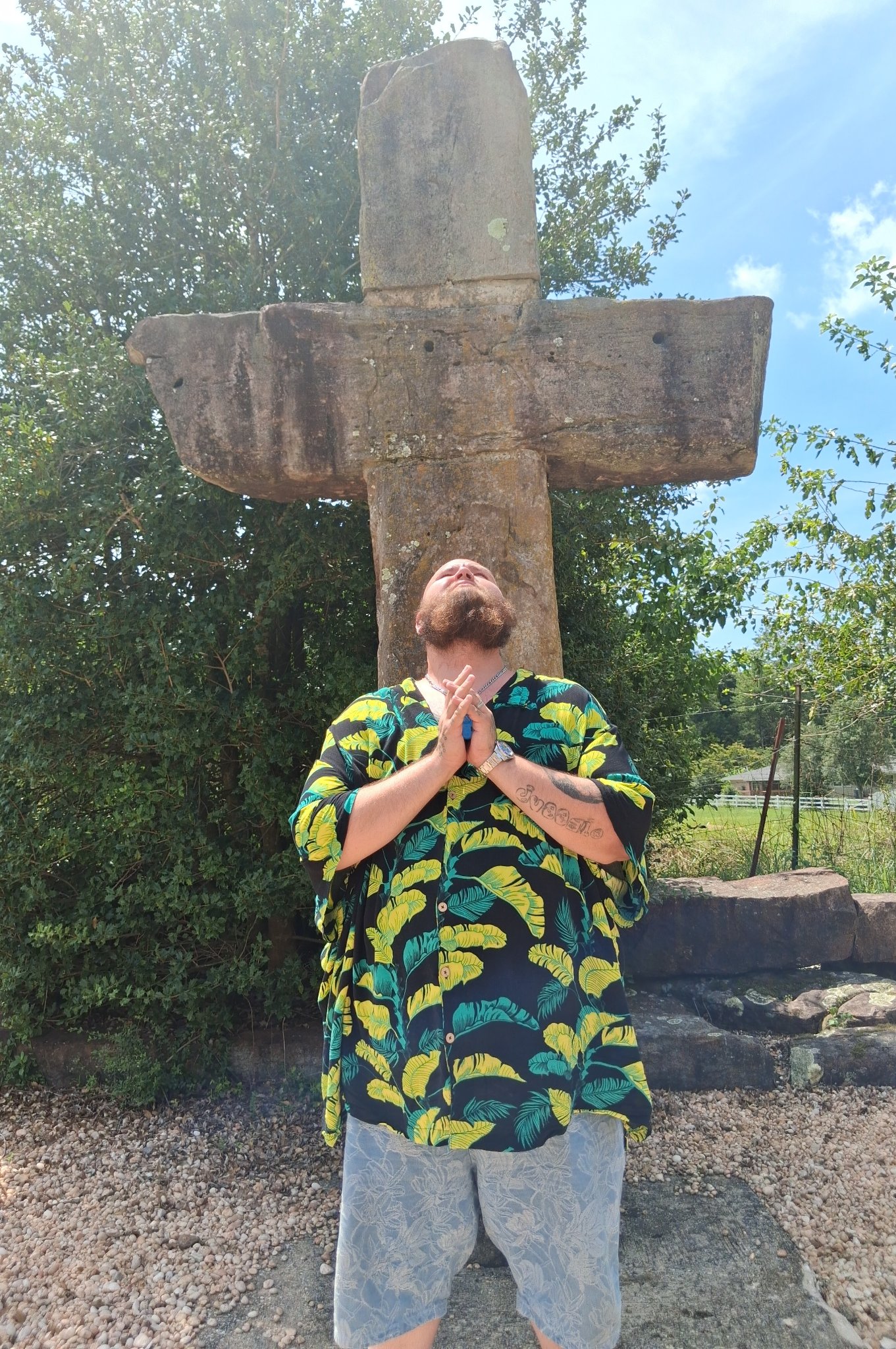 Man standing in prayer beneath a large stone cross at Stonehenge Kentucky